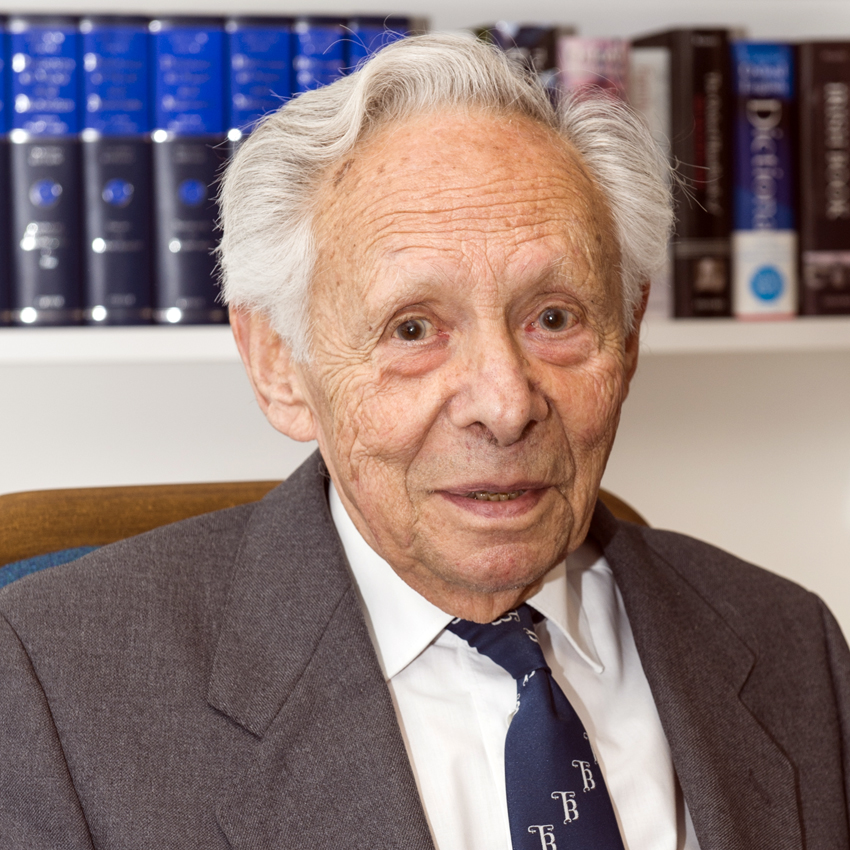 Eldery white man in suit and tie in fron of bookshelf